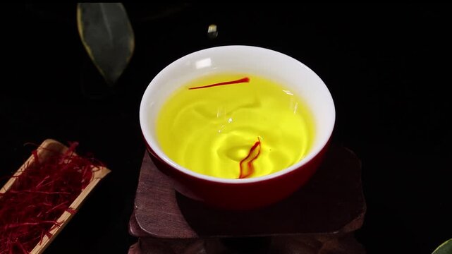 Slow motion shot of a water drop falling into a cup of saffron tea
