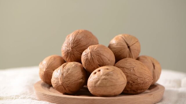 Close-up shot of a small pile of fresh raw walnuts arranged on a wooden plate, natural textures and neutral background