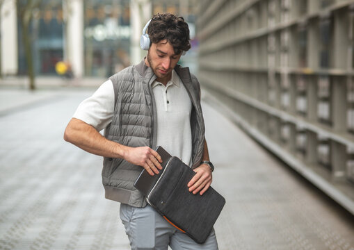 Man putting laptop into sleeve wearing headphones urban area