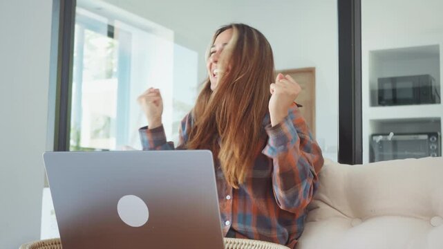 surprised and happy woman reacting to laptop screen at home hands on face showing excitement. surprised woman receiving good news online while working remotely in modern apartment
