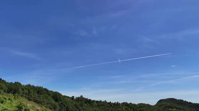 Cielo azzurro con scie aeree sopra colline verdi ricoperte di vegetazione fitta. Una scena naturale luminosa con un tocco di movimento nel cielo