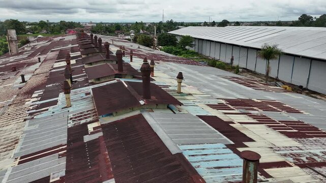 An aerial view showing the roof of an old factory made of rusted corrugated metal, with several rusted smokestacks.