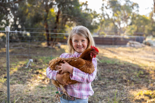 Caucasian girl standing outdoors holding a brown chicken with red comb