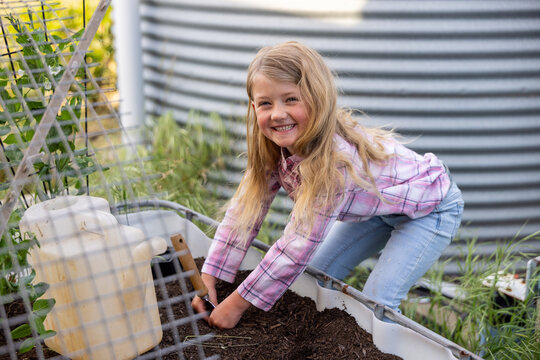 Child with long blonde hair, hands working in dirt using shovel
