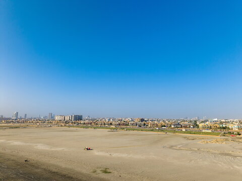 Aerial view of Sea-View Beach with sandy coastline, urban buildings in the distance, and clear blue sky in Karachi, Sindh, Pakistan.