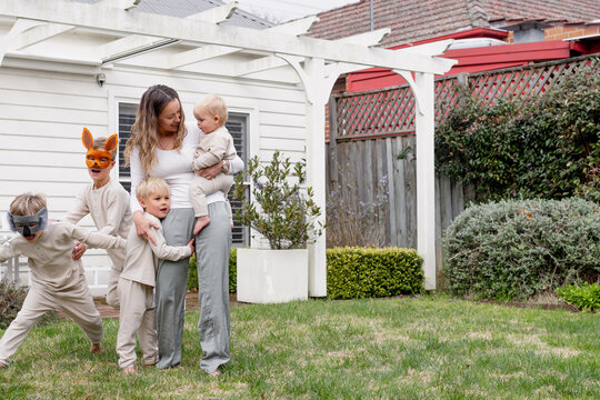 Young boys running around mum holding a baby in the garden