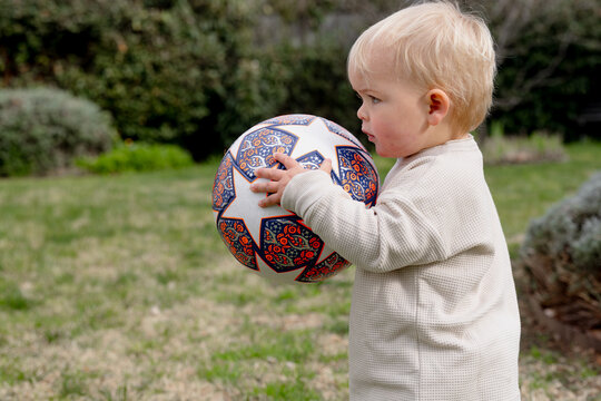 Toddler boy holding a soccer ball in the backyard