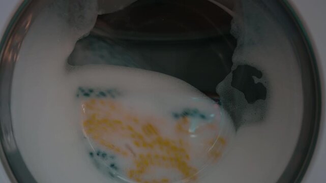 Clothing and soapy water spin around in machine. Washing machine door. Front loader