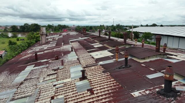 An aerial view showing the roof of an old factory made of rusted corrugated metal, with several rusted smokestacks.