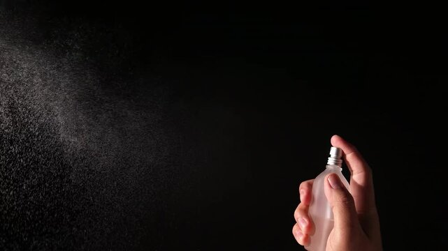 Hand Spraying perfume from Spray Bottle on Black Background
