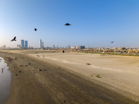 Aerial view of Sea-View Beach with birds flying over the sandy shore and the city skyline in the background in Karachi, Sindh, Pakistan.