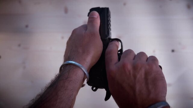 Close-up of hands manipulating and loading a black pistol, symbolizing danger, weapon trafficking, and criminal intent in a cinematic low-key lighting.