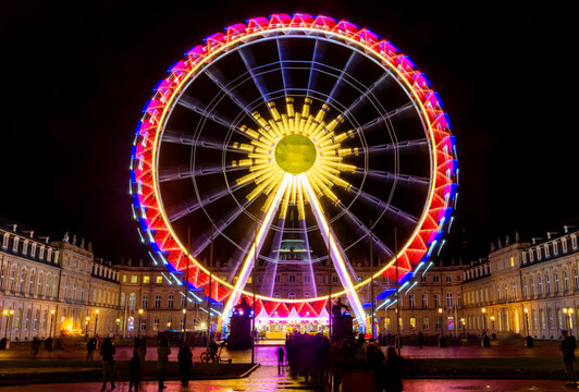 Giant ferris wheel on the &ldquo;Schlossplatz&ldquo; central square in the heart of Stuttgart Germany. Nighttime atmosphere at christmas with roundabout in motion. New Palace landmark monument in the background.