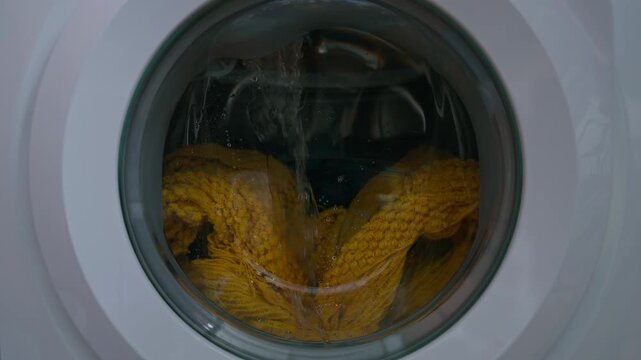 Clothing and soapy water spin around in machine. Washing machine door. Front loader