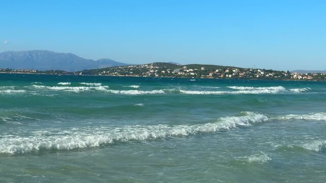 Gentle sea waves rolling toward the shoreline on the Cesme coast. Natural Mediterranean seascape with clear water, relaxing movement, summer travel atmosphere, and coastal tourism scenery.