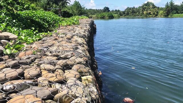 Scenic landscape of a rock gabion retaining wall along a calm river bank