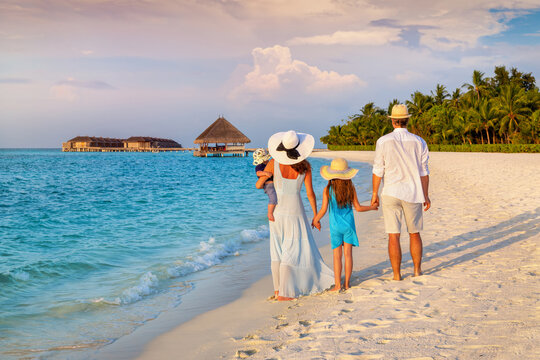 Rear view of a family on vacations looking at a tropical paradise beach in the Maldives islands during sunset time