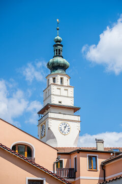 The town hall tower is situated in the center of Boskovice, Czechia. It is a clear day with a blue sky and a few clouds in the background. The tower shows the time on its clock face.