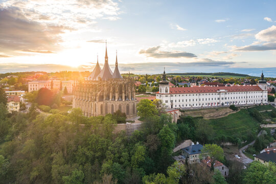 This aerial view shows Saint Barbara's Church and Jesuit College during the evening in Kutna Hora, Czechia. The sun sets behind the historic buildings and green trees.