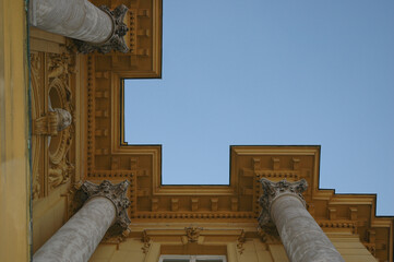 Low angle looking up at a neoclassical building facade with prominent geometric roof cornice molding and decorative columns under blue sky. © nahhan