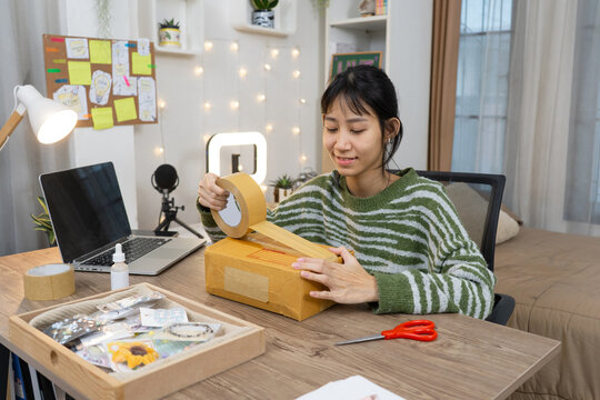 Young online seller Owner Packing Orders with packing tape,  preparing customer orders in home Studio office