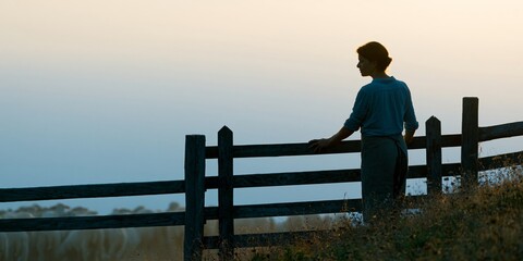 Fototapeta premium Woman standing by wooden fence at dusk