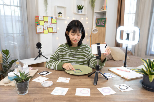 Young Online Seller Presenting Handmade Jewelry  during a live stream with smartphone and ring light setup in Home Studio Workspace