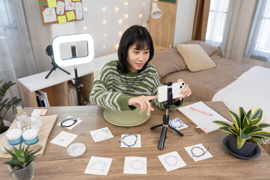 Young Online Seller Hosting Live Stream and Engaging with Customers with smartphone and ring light setup in Home Studio Workspace