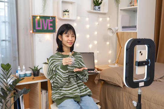 Young online seller Recording Presenting Skincare Product to Mobile Camera and Ring Light Setup for Social Media Marketing