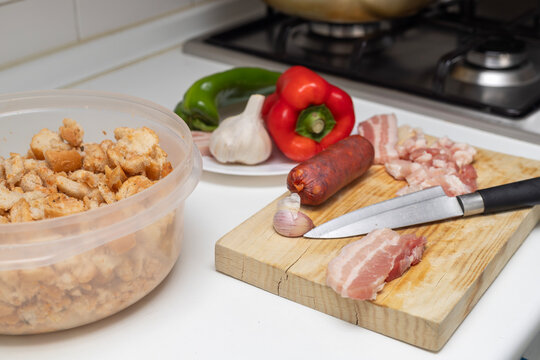 Slicing pork belly and bread for spanish migas ingredients on a kitchen counter