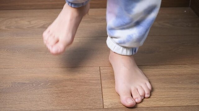 Teenager stomping feet on wooden floor during emotional outburst at home. Close-up of bare feet expressing frustration, protest, anger, conflict and stress