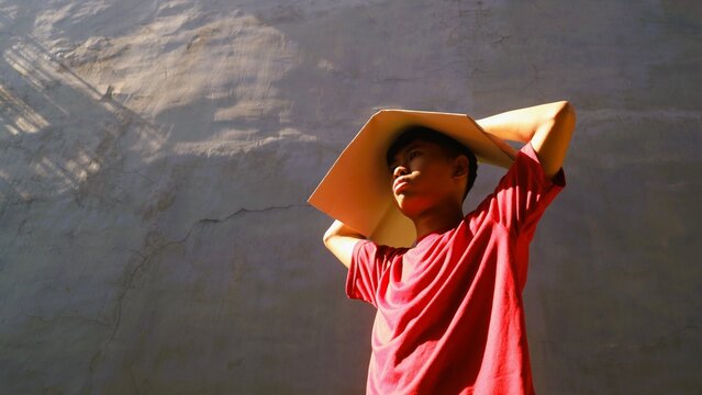Young man shielding face from extreme heat with a cardboard sheet outdoors