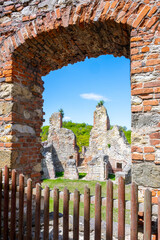Fototapeta premium Visitors look through an archway at the ruins of Boskovice Castle. The remains show the historical structure against a clear blue sky. Green trees surround the area, marking the landscape.
