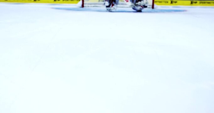 Close up of a hockey stick blade on ice moving a black rubber hockey puck across the surface in a rink
