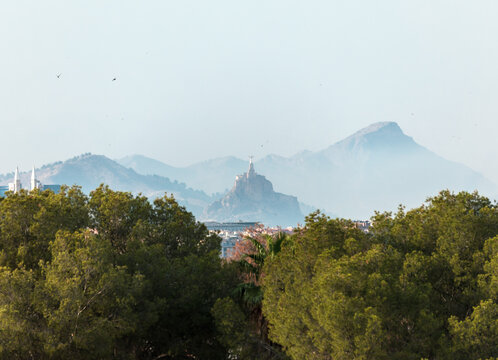 The medieval castle of Monteagudo, Murcia, Spain, seen from a distance through the mist and trees