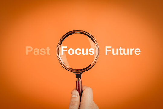 Hand holding magnifying glass focusing on the word Focus between Past and Future. Concept of mindfulness, vision, and time management.