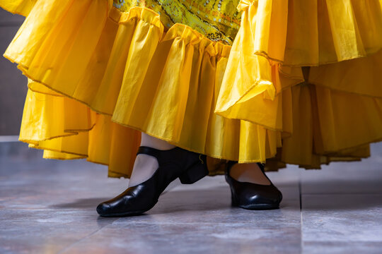 Character dancer feet in black stage shoes and ruffled yellow skirt close up on tiled floor