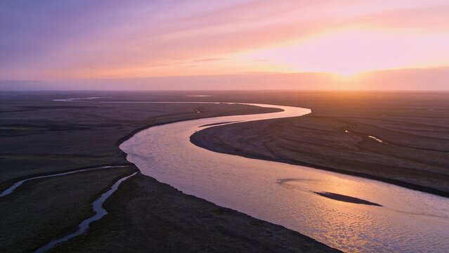 Meandering river channel snaking across wetland plain, reflecting sunset colors and sandbars