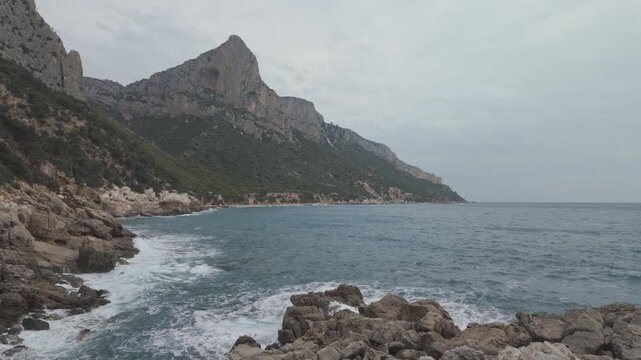 Waves rolling onto rocky coastline below Pedra Longa cliffs in Sardinia