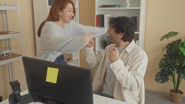 Man and woman embrace over computer monitor, smiling and arms wrapped around each other in building; joy teamwork.