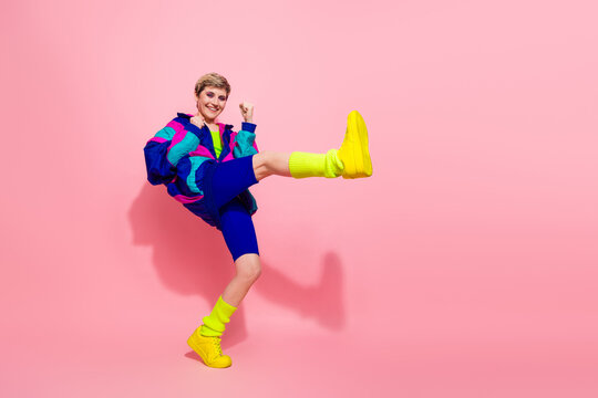 Young stylish woman in retro fitness attire posing on vibrant pink background, showcasing energy, style, and fitness