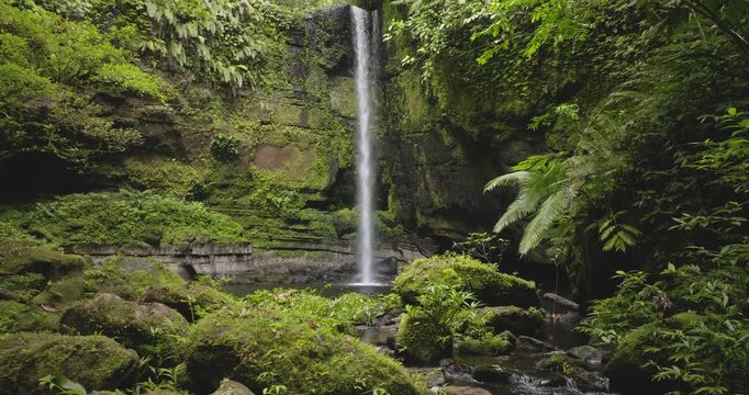 Travel and explore Solomon Islands. Waterfall streaming down a moss covered cliff face, vibrant green jungle foliage and large rocks covered in verdant moss, creating a serene and wild nature scene