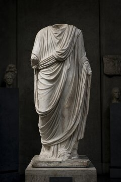 A headless marble statue with detailed toga folds in a museum setting.