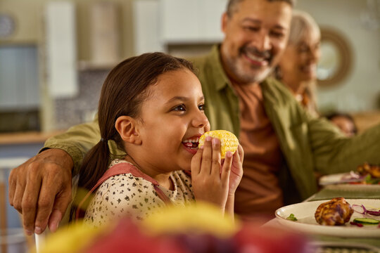 Cute little girl eating an ear of corn at lunch