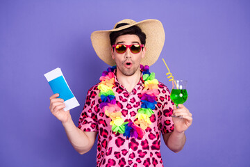 Young man in tropical attire holding travel documents and a drink, wearing sunglasses and a straw hat against a purple background © deagreez