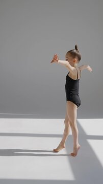 Little Caucasian girl gymnast in a black leotard posing on a white background. 