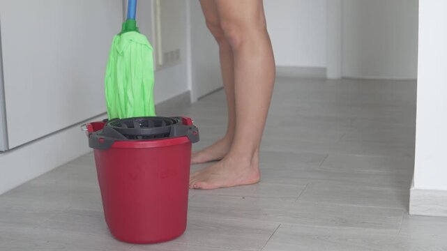 Woman wringing a mop into a bucket while cleaning the floor at home. Close-up domestic scene with housework, wet floor cleaning and everyday home hygiene routine