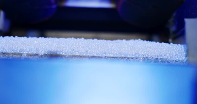 Plastic pellets moving across a vibrating blue metal screen in an industrial factory production line