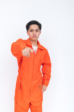 Young male seafarer in orange coveralls pointing toward the camera with a serious expression, conveying attention, responsibility, warning, or direct communication.