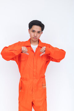 Young male seafarer in orange coveralls displaying a double thumbs down gesture with a serious expression, symbolizing disapproval, dissatisfaction, or rejection.